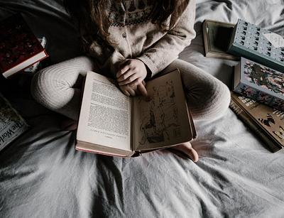 child sitting on a bed surrounded by books